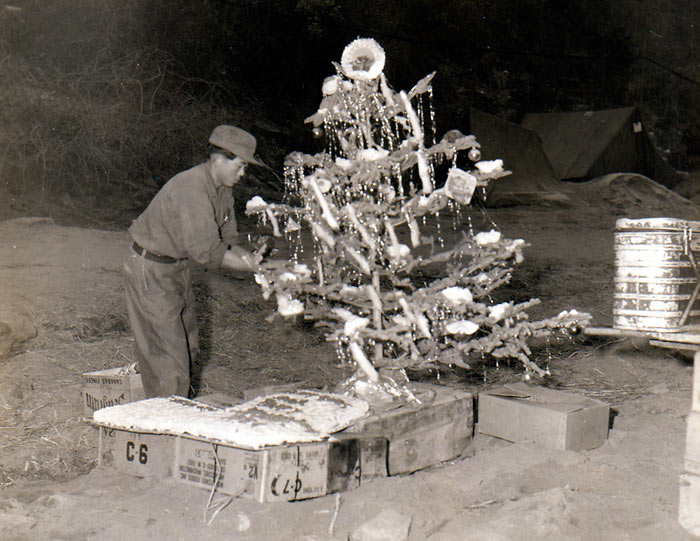 Korean KP decorates Christmas tree set up in front of serving counter of HQs & HQs Co, 19th Inf Regt, 24th US Inf Div, as Christmas Day dinner is readied for men of the Co. Korea. 25 December 1951.