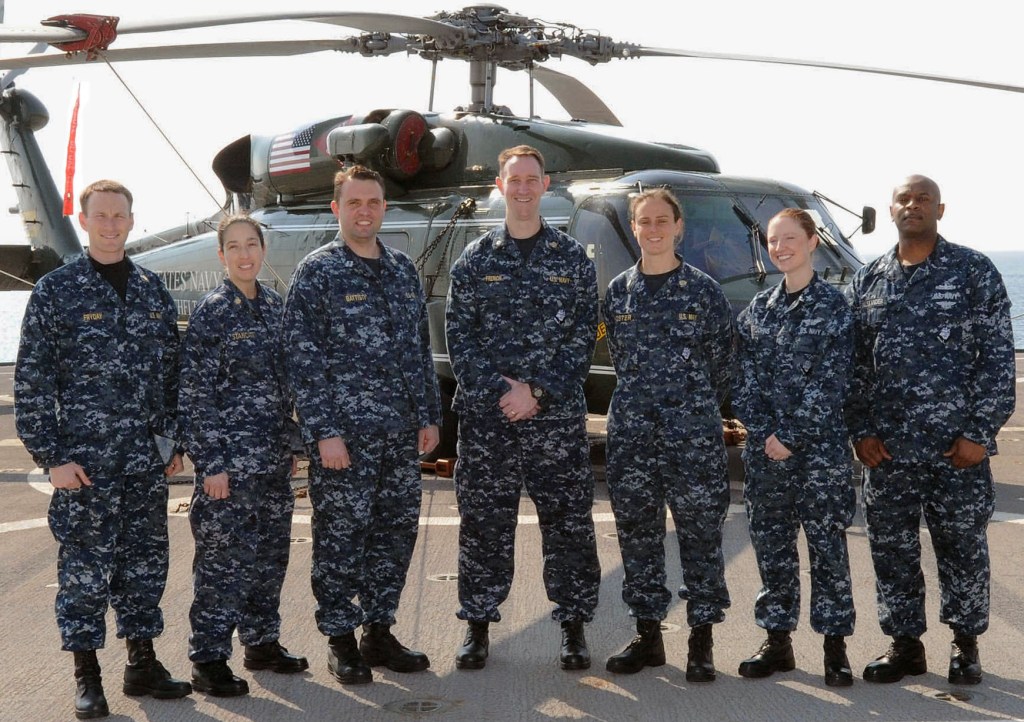 Group of military personnel in front of helicopter.