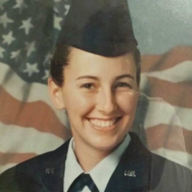 Photo of a smiling young Christy in service uniform, in front of American flag. U.S. Air Force. Morro Bay High Grad.
