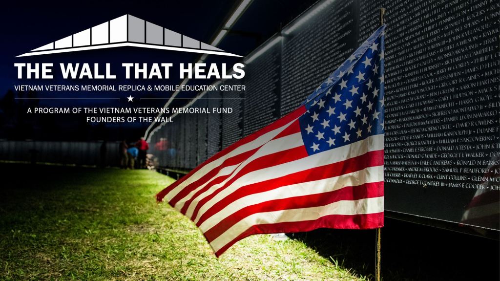 Photo of the mobile replica of the Vietnam Veterans War Memorial with text that reads: The Wall That Heals. An American flag flies in the foreground.