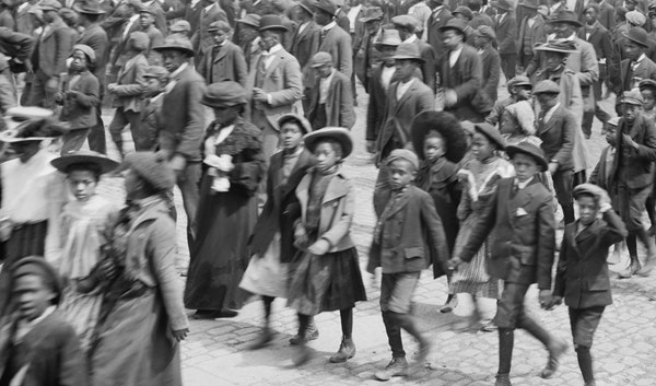 Black and white photo of African Americans parading down a street celebrating Juneteenth.