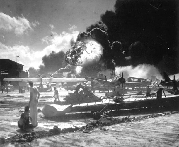 U.S. sailors stand among wrecked airplanes at Ford Island Navel Station during the attack on Pearl Harbor.