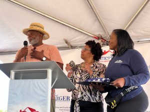A man using microphone to talk on stage standing next to two women.