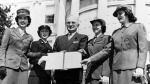 President Harry S. Truman holds up a signed document with four women in military uniform.