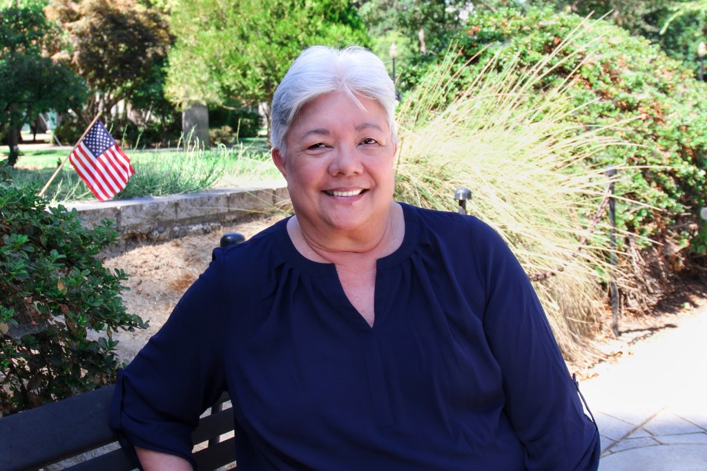 Woman outside on park bench with small American flag in background.