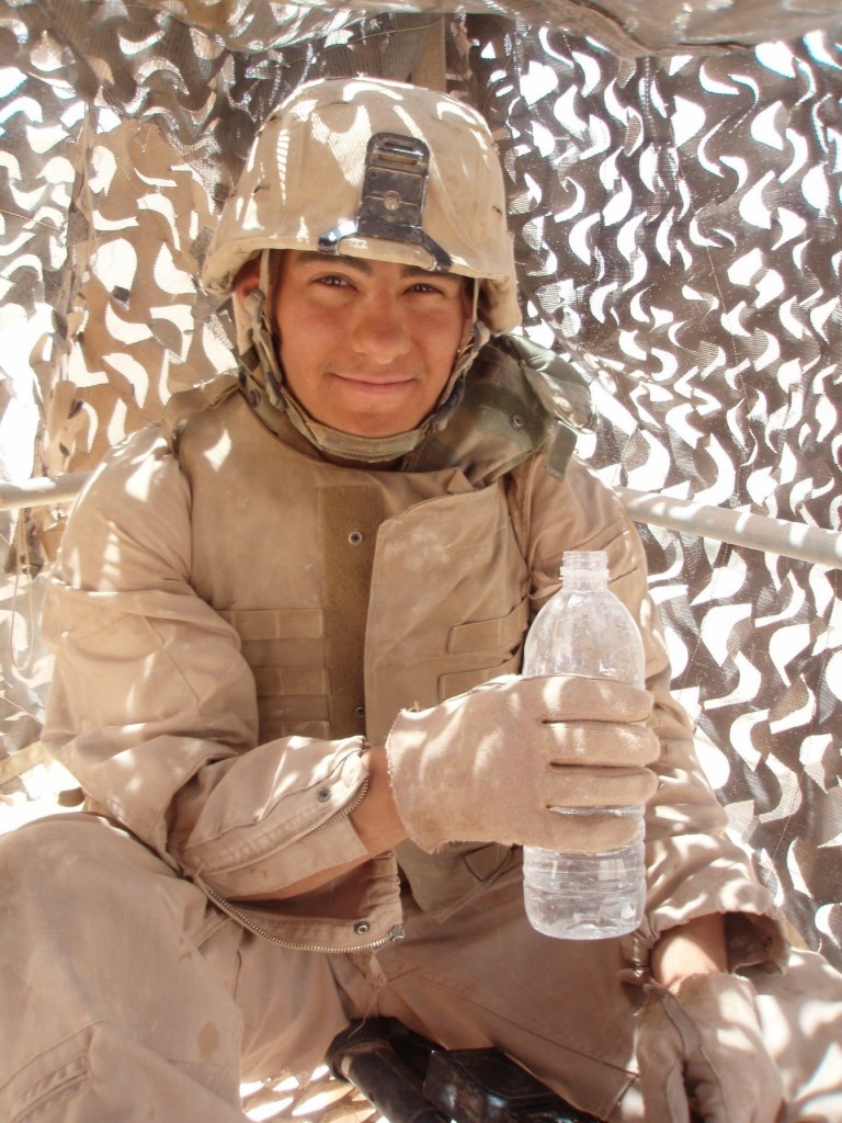 Servicemember in Iraq wearing combat gear and holding water bottle..