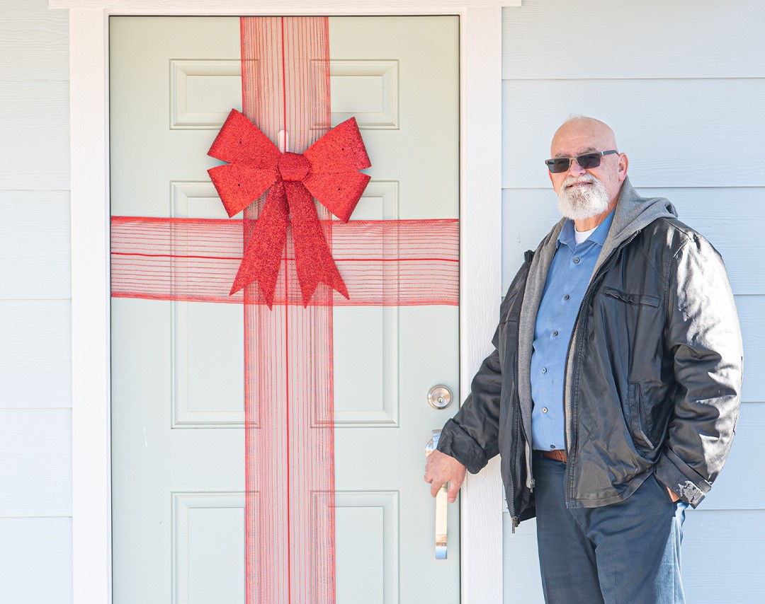 Man standing outside door of house, with red ribbon and bow on the door.