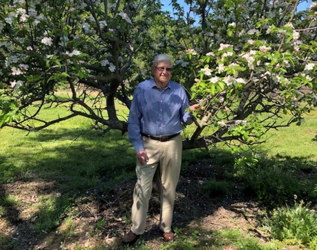 Man standing outside in front of apple tree.