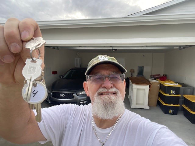 Man holding up keys with home's garage in background.