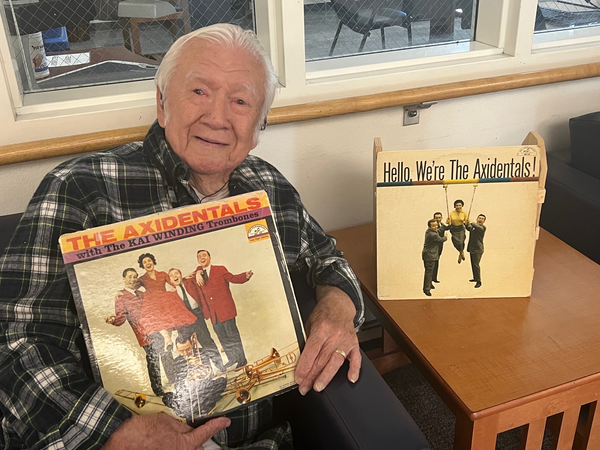 Seated man holds music record with another record on table nearby.